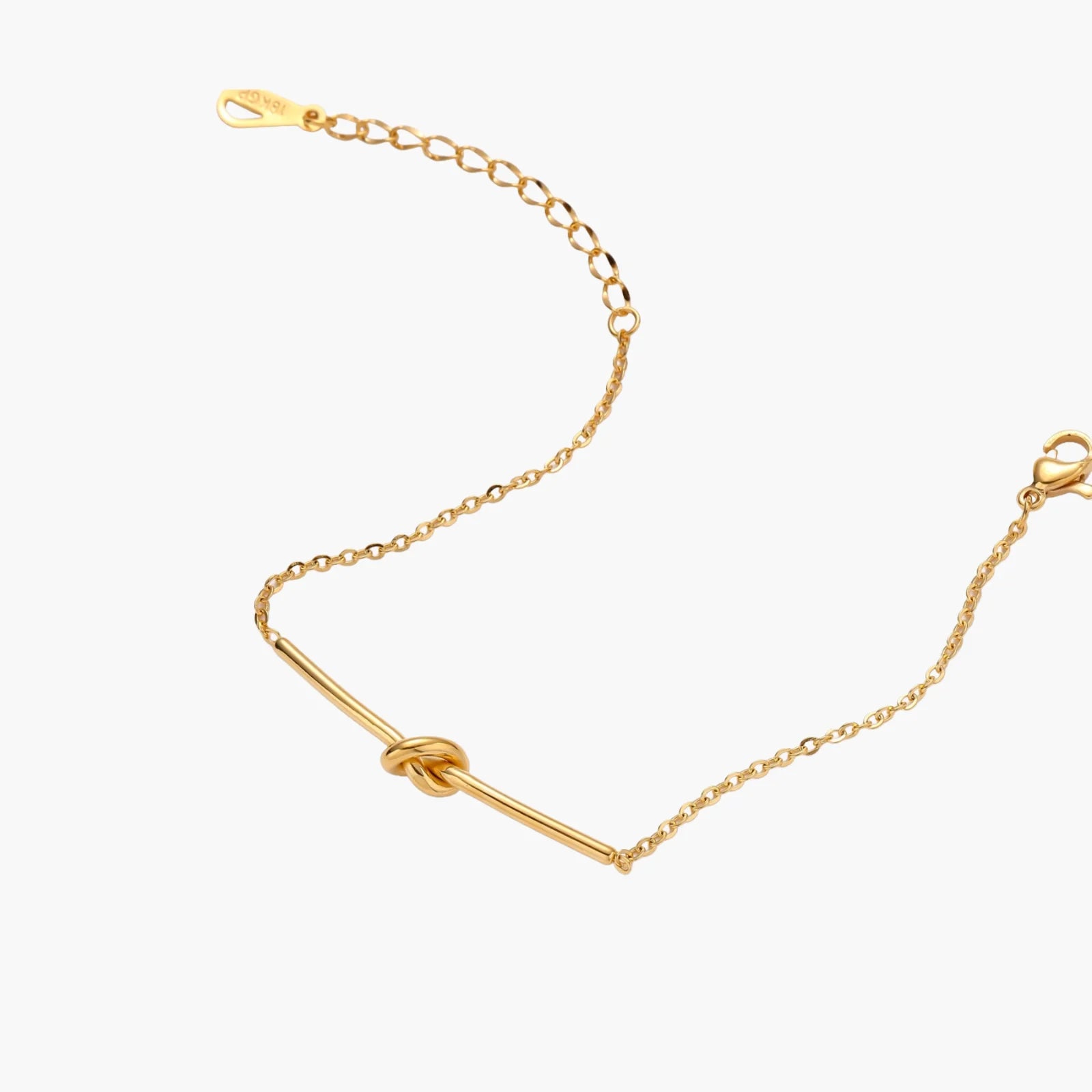 Delicate gold chain bracelet with minimalist bar and centered knot detail on cream background