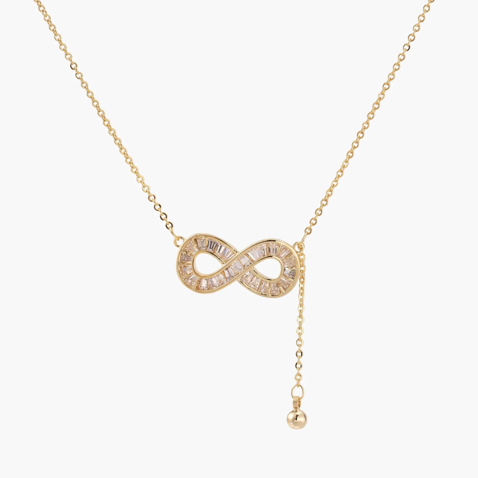 Gold infinity pendant with baguette crystals on adjustable chain against cream background.